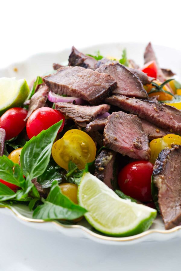 Slices of grilled steak in a salad plate with lime and tomatoes.