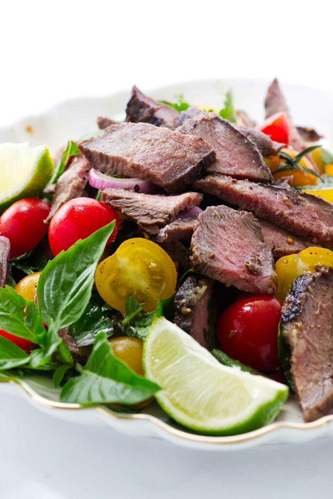 Slices of grilled steak in a salad plate with lime and tomatoes.