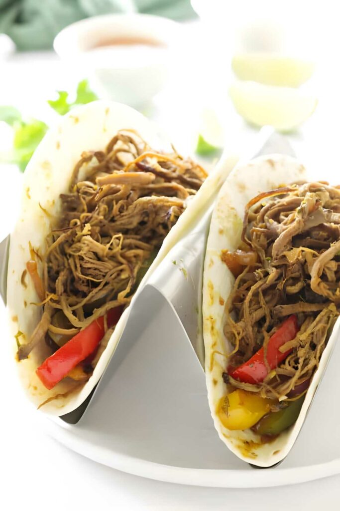 Two fajitas with shredded meat and peppers in a white taco holder.