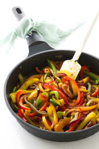 Colorful bell peppers sautéed in black pan with white spatula and blue cloth.