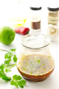 Small jar of brown vinaigrette with cilantro, lime, chili, and spices.