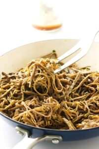 Shredded tri tip, cooked jackfruit in white skillet stirred with fork, bright background.