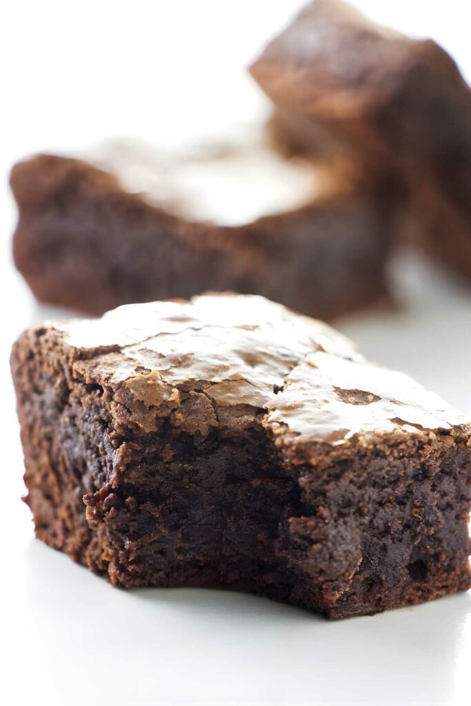 A bitten chocolate brownie showing fudgy center and crackle top.