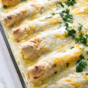Cheesy baked chicken enchiladas with white sauce in glass dish.