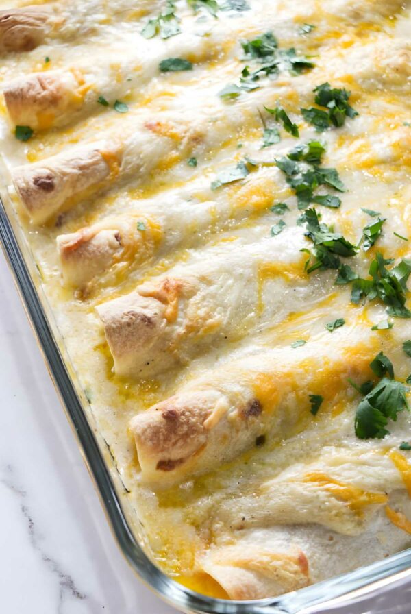Cheesy baked chicken enchiladas with white sauce in glass dish.