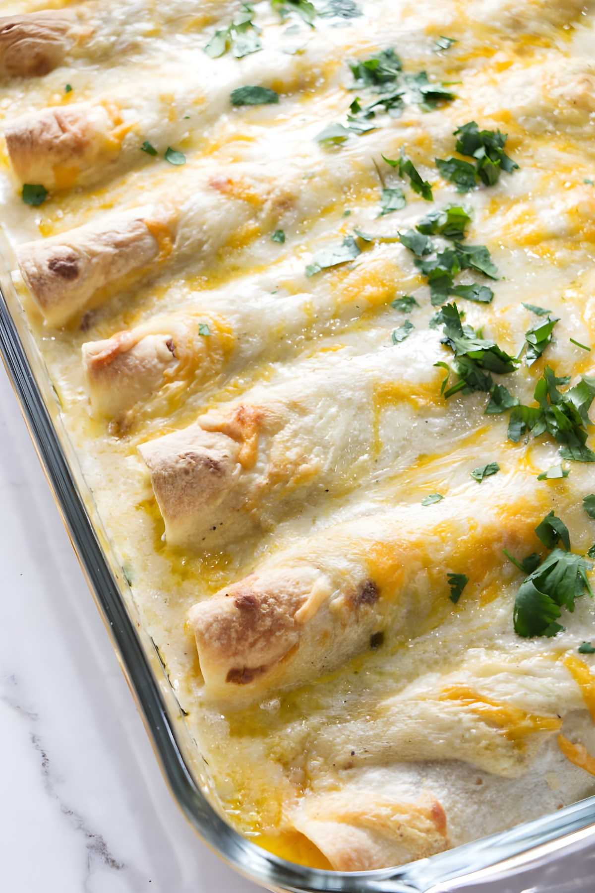 Cheesy baked chicken enchiladas with white sauce in glass dish.