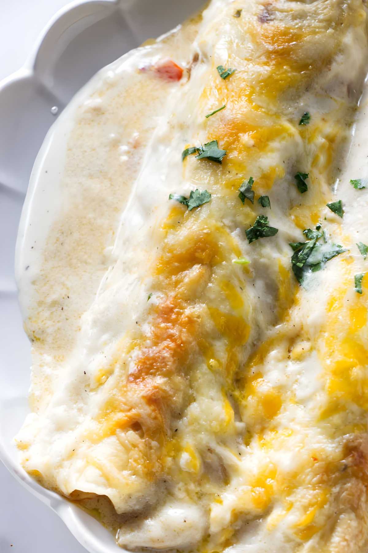 Two cheesy baked chicken enchiladas with white sauce and herbs on a plate.