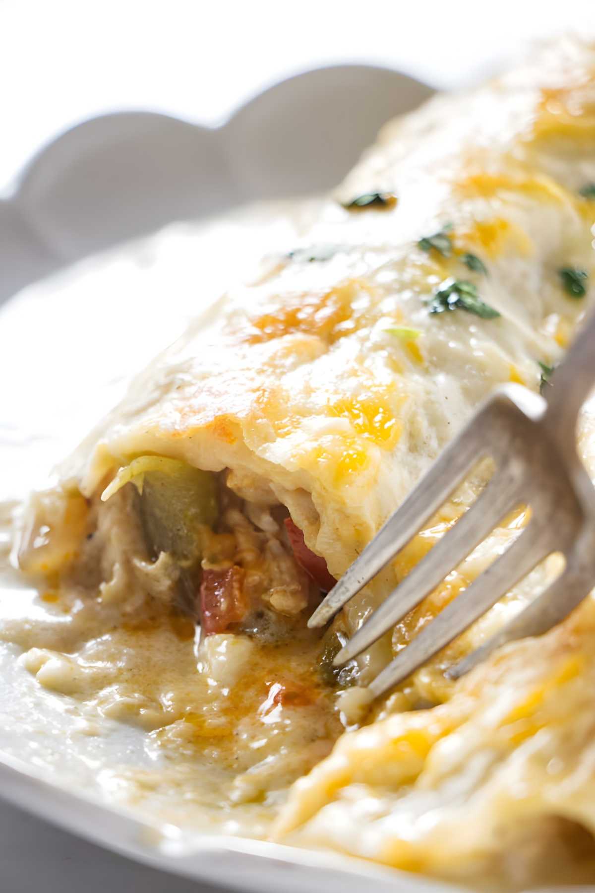 Close-up of creamy chicken enchilada with green chile being cut with a fork.
