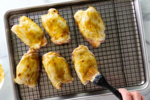 Brushing chicken thighs with a sweet glaze.