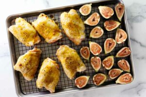 Fresh figs and chicken thighs on a baking sheet.