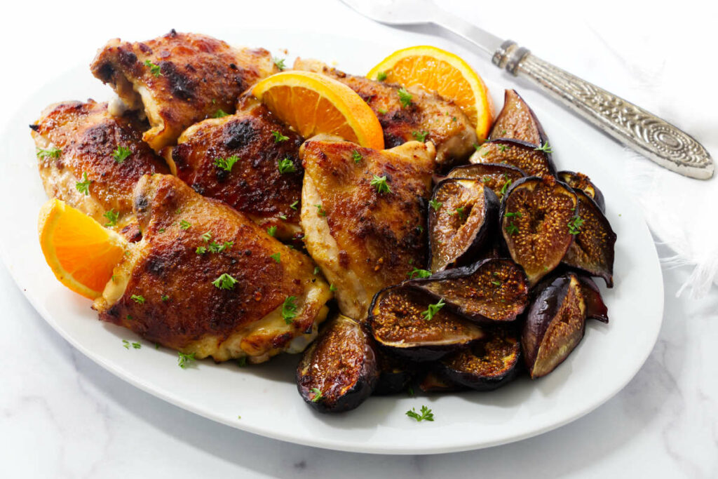 Sheet pan chicken and figs with orange wedges on a plate.