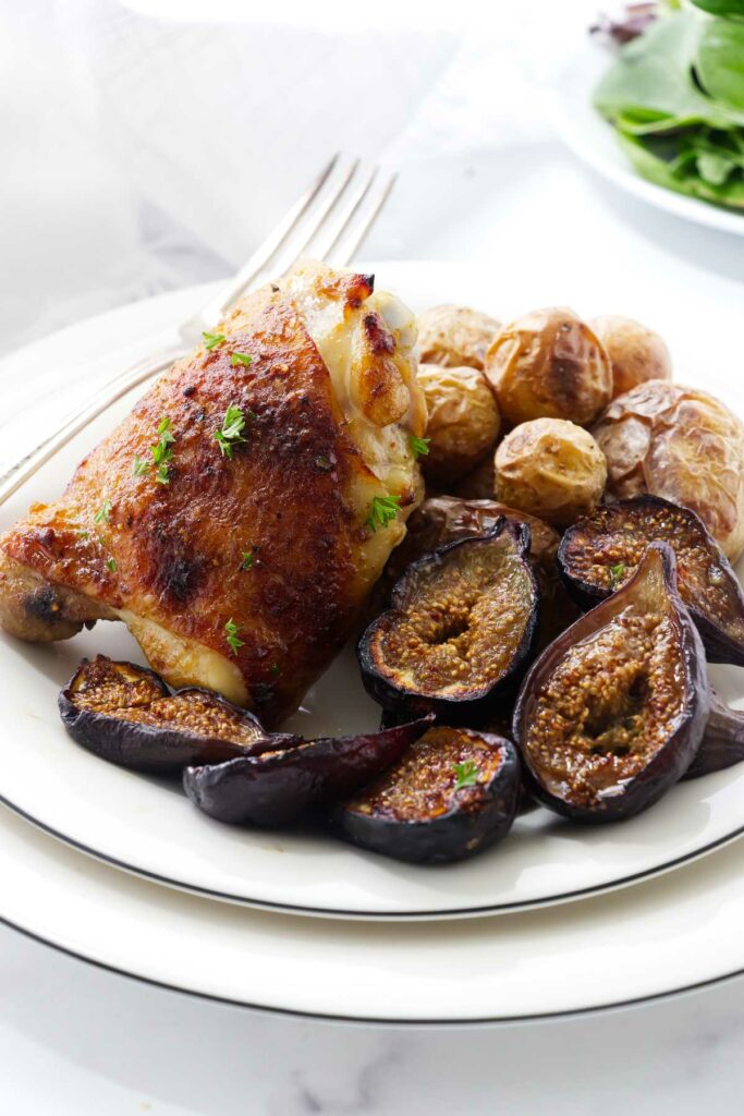 A baked chicken thigh and figs on a plate with potatoes.