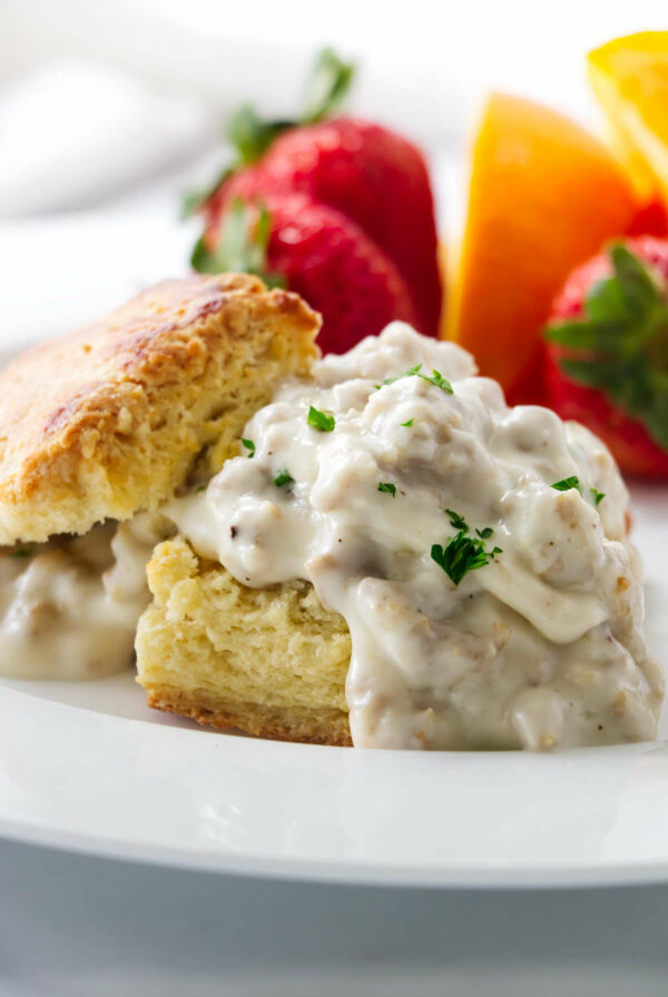 Biscuits and gravy on a plate with strawberries and oranges.