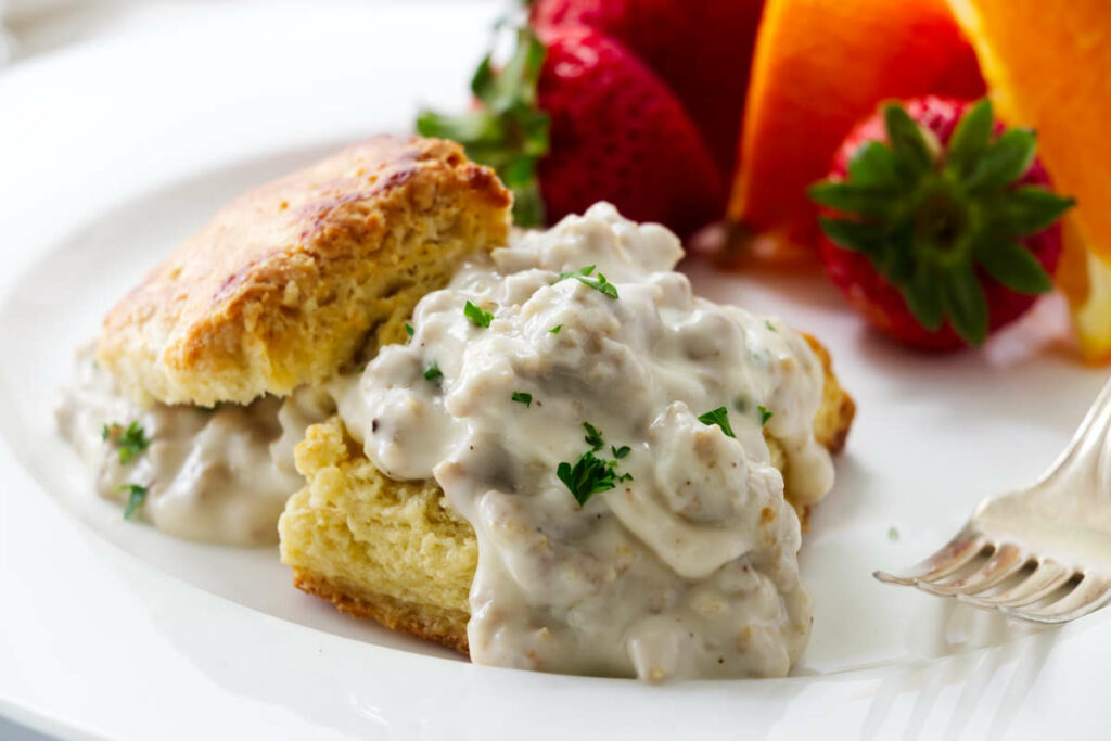 Sausage gravy on a biscuit and fruit in the background.