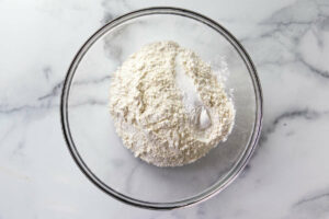 Combining flour, salt, and baking soda in a mixing bowl to make biscuits.