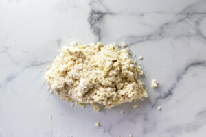 Pushing biscuit dough into a mound on a counter.