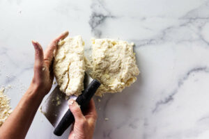 Cutting the biscuit dough and folding it over itself to make flaky layers.