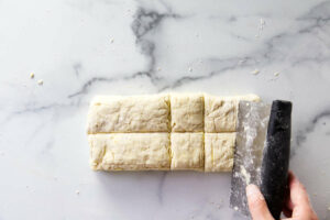 Slicing biscuits on a counter with a bench scraper.