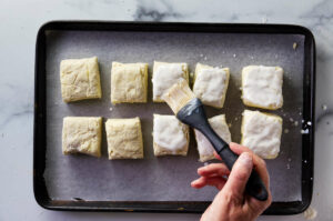 Brushing cream on top of homemade buttermilk biscuits.