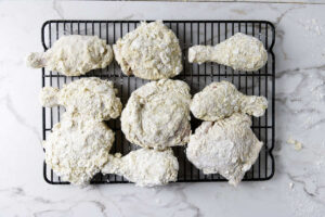 Several chicken pieces sitting on a rack after getting dredged.