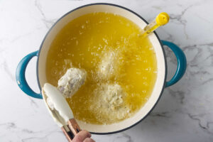Adding coated buttermilk chicken pieces to hot oil.
