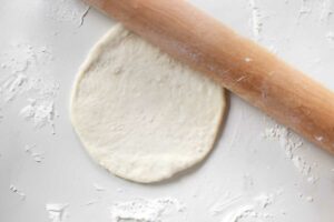 Rolling dough into a flat circle to fry.