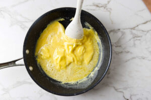 A spatula stirring scrambled eggs in a skillet.