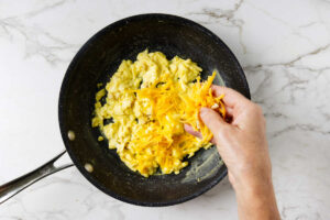 Adding shredded cheese to soft scrambled eggs in a skillet.