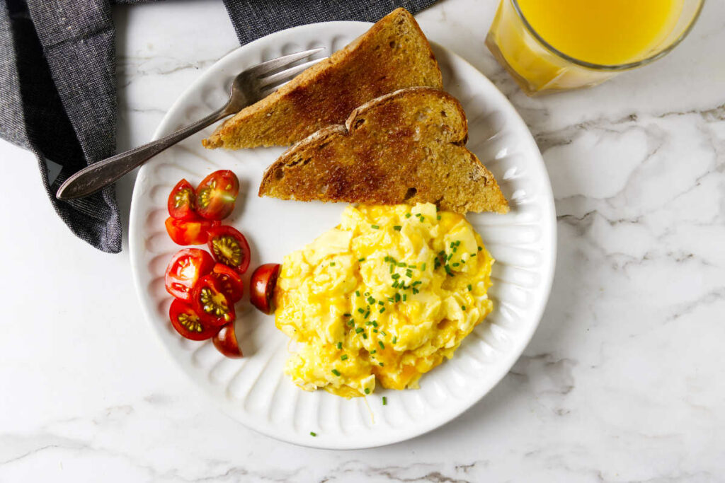 Scrambled eggs with cheese on a plate with sliced tomatoes and toast.