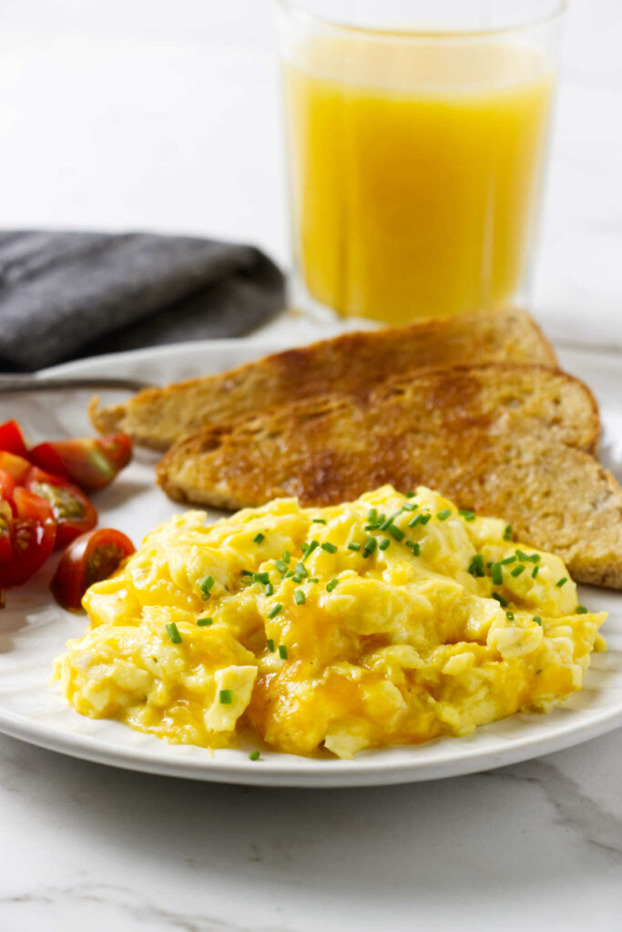An egg and cheese breakfast scramble on a plate with toast and tomatoes.