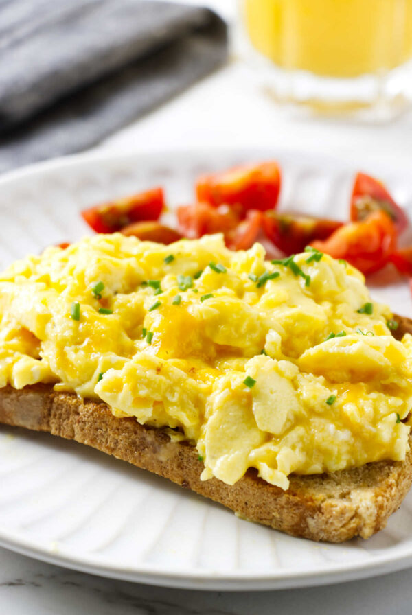 Scrambled eggs with cheese on a slice of toast; tomatoes and orange juice in the back.