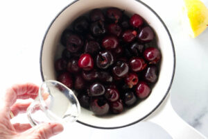 Adding lemon juice to a sauce pan with cherries.