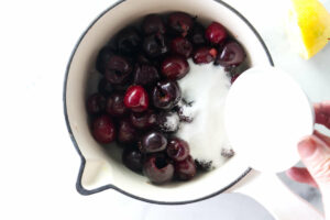 Adding sugar to a sauce pan with cherries.