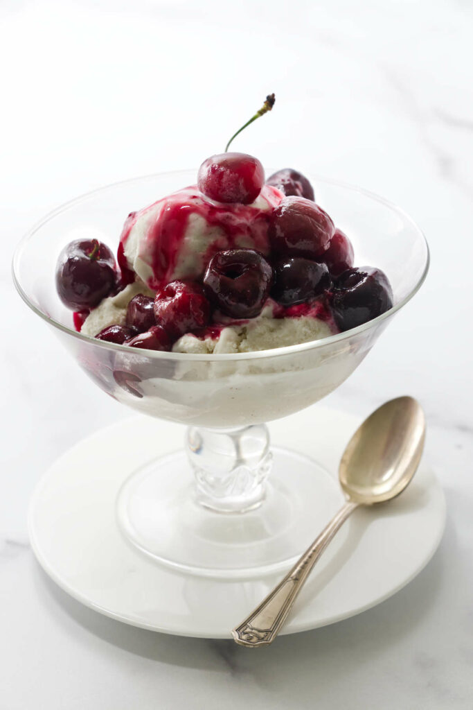 Cherry compote sauce on a scoop of ice cream in a bowl.