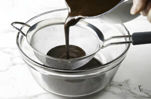 Straining the ice cream custard through a metal sieve.