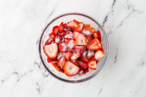 Combining strawberries with sugar in a bowl.