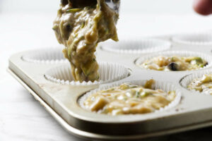 Adding muffin batter to a muffin tin; grated fresh zucchini in the batter.