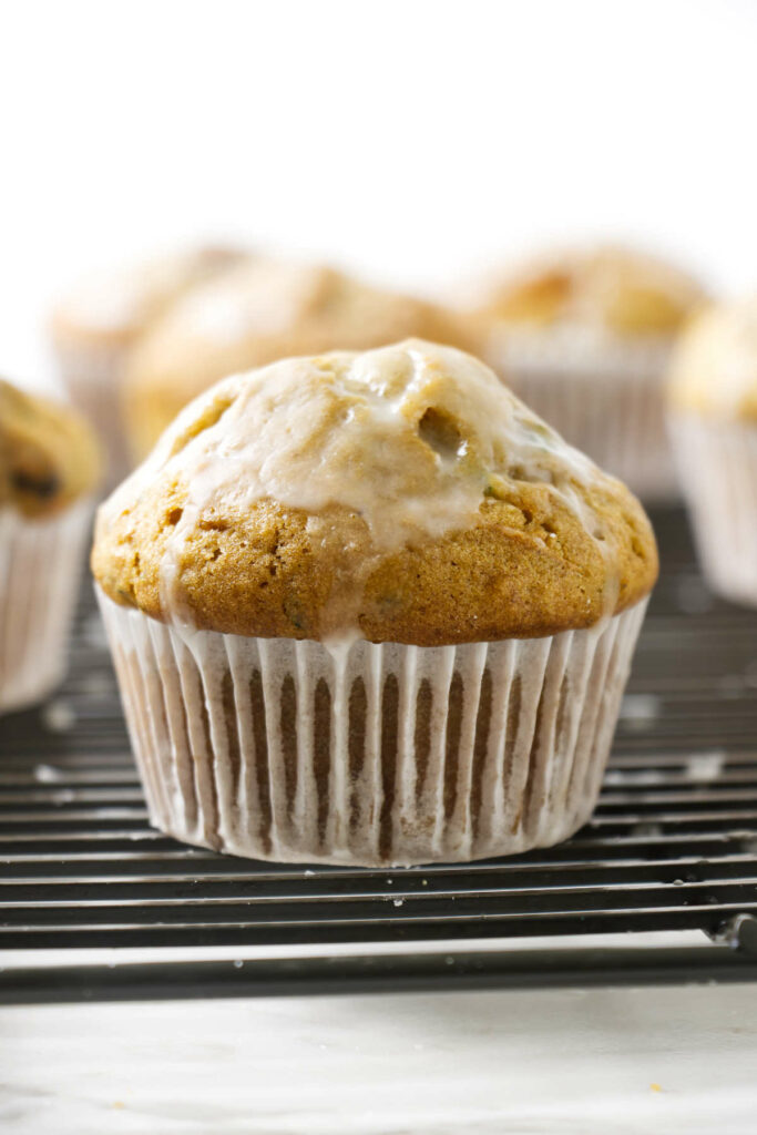 An iced zucchini muffin on a bakers rack with a paper cupcake liner.