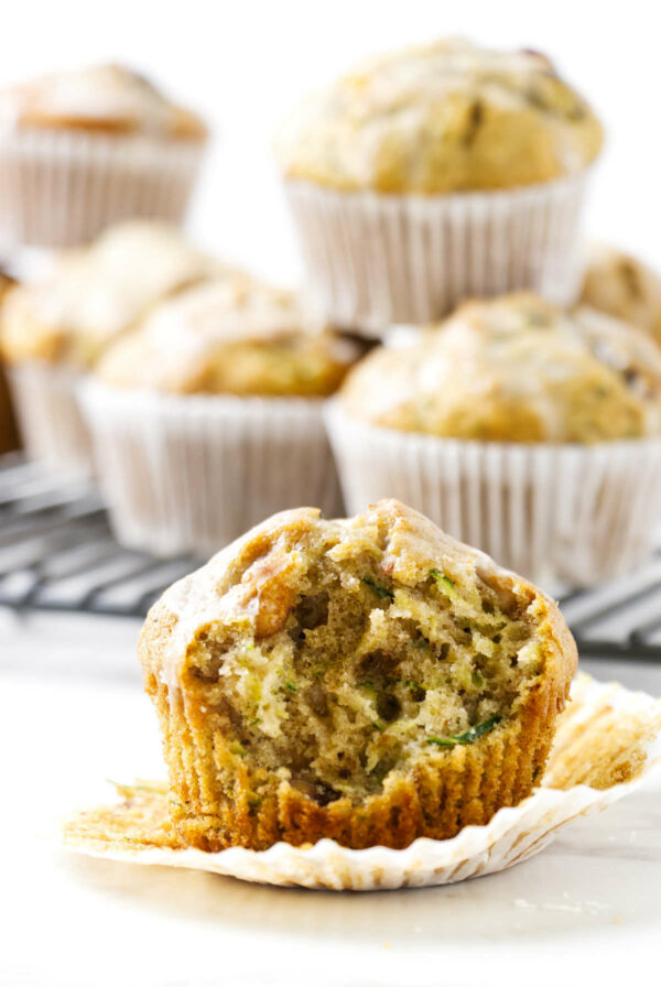 A partially eaten zucchini muffin next to more muffins on a cooling rack.
