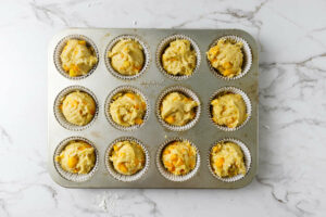Dividing muffin batter into a muffin tin with twelve wells.