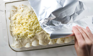 Covering a casserole dish with foil to bake enchiladas with crab.