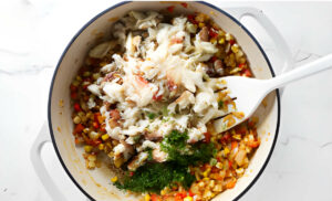 Adding crab meat to a skillet with enchilada filling.