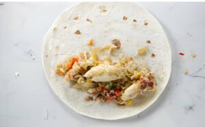Adding lump crab meat and enchilada filling to a tortilla.