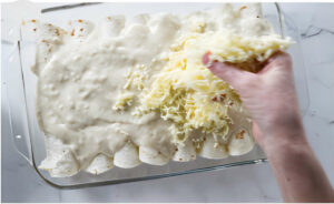 Sprinkling cheese over crab enchiladas in a casserole dish.