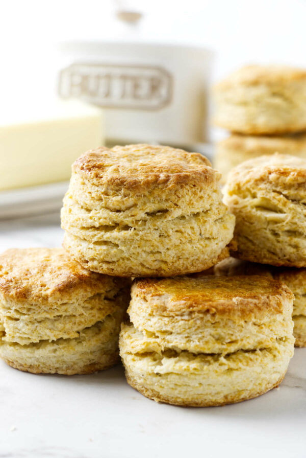 Flaky golden biscuits in front of a container of butter.