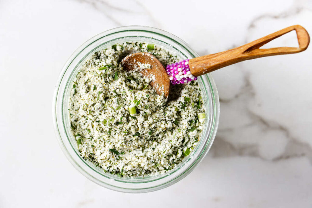 A spoon in a jar of dry ranch dressing seasoning.