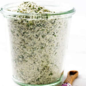 A jar filled with a homemade ranch seasoning next to a wooden spoon.