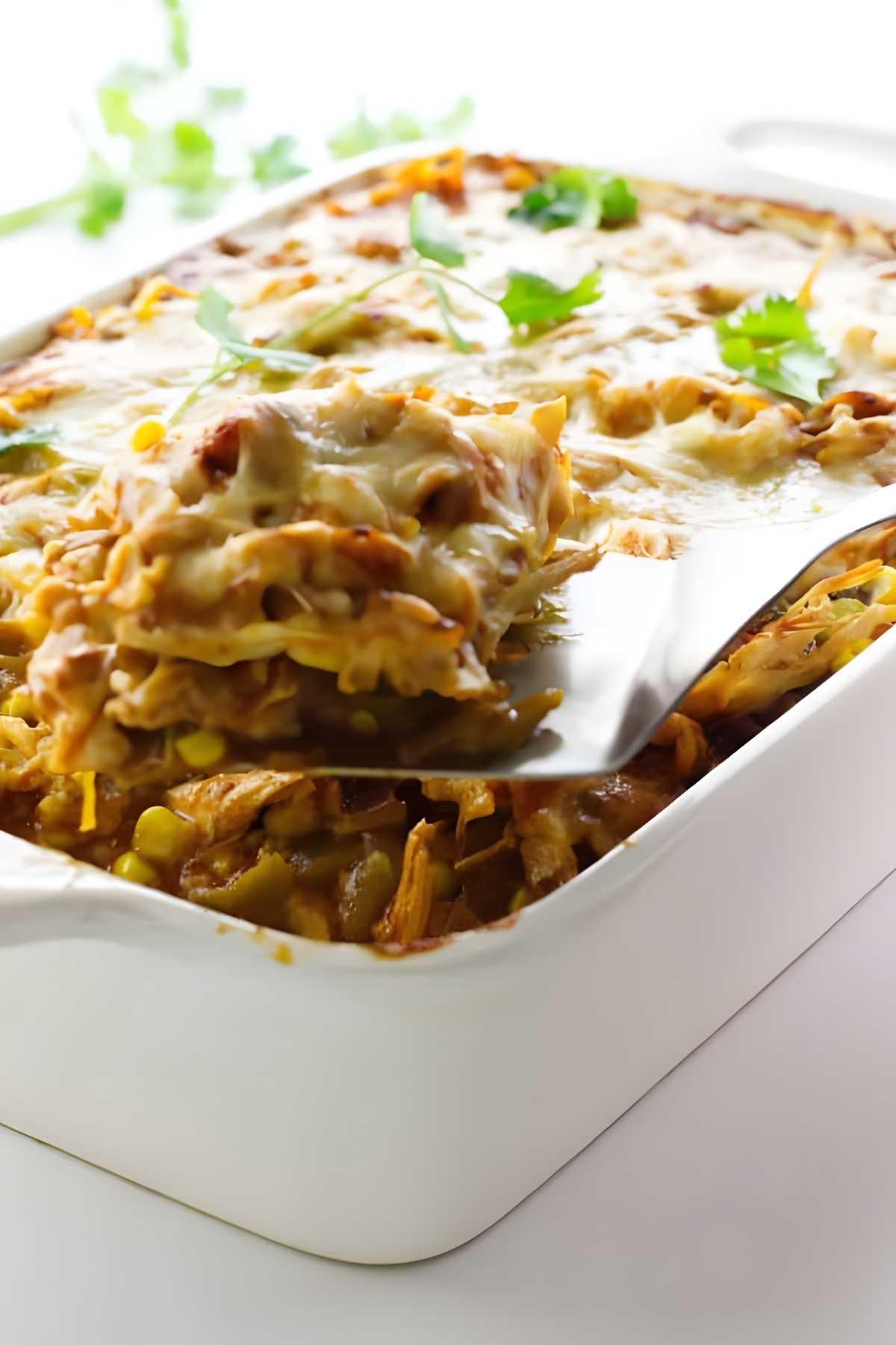 A spatula lifting a slice of polenta enchilada from a casserole dish.