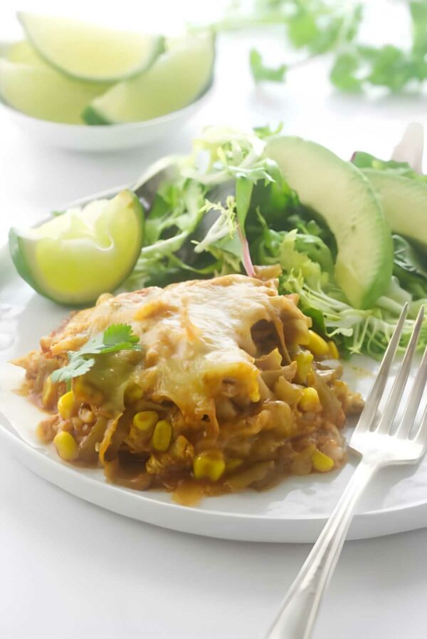 A serving of polenta chicken enchilada on a plate with avocado slices.
