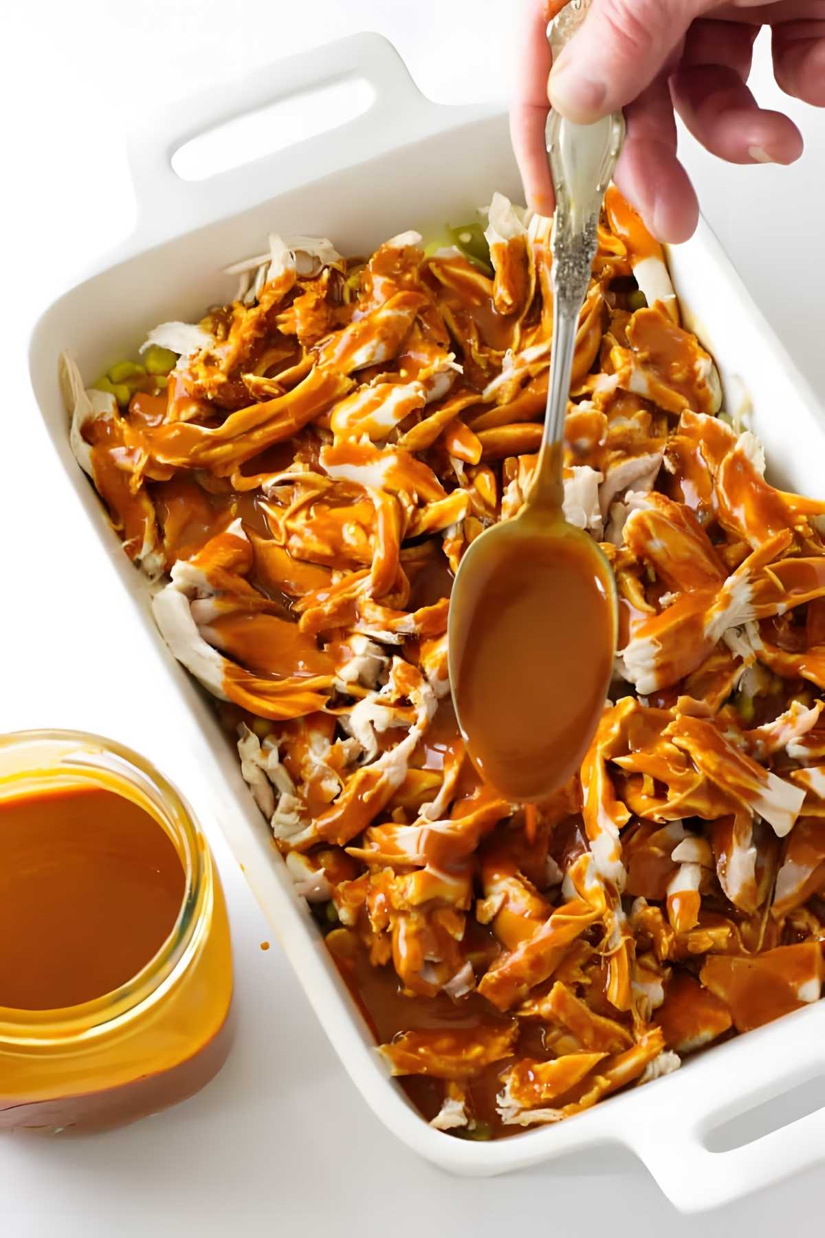 Pouring enchilada sauce over shredded chicken in a casserole dish.